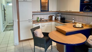 Cocina compacta con alacenas blancas, cafetera, hervidor y pileta.