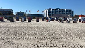 Una playa con sillas y sombrillas, un edificio de varios pisos y banderas.