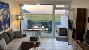 Una sala de estar moderna con un sofá, una mesa de comedor y un balcón con vistas al mar.