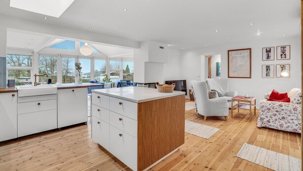 A modern kitchen with white cabinetry, a wooden island, and a large window overlooking a garden.