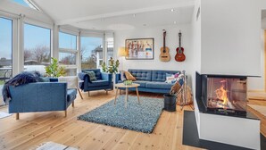 A modern living room with a fireplace, blue sofas, and a large window overlooking a snowy landscape.