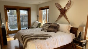 Ein Schlafzimmer mit einem großen Bett, Holzboden, einem an der Wand befestigten Kruzifix und Blick ins Freie.
