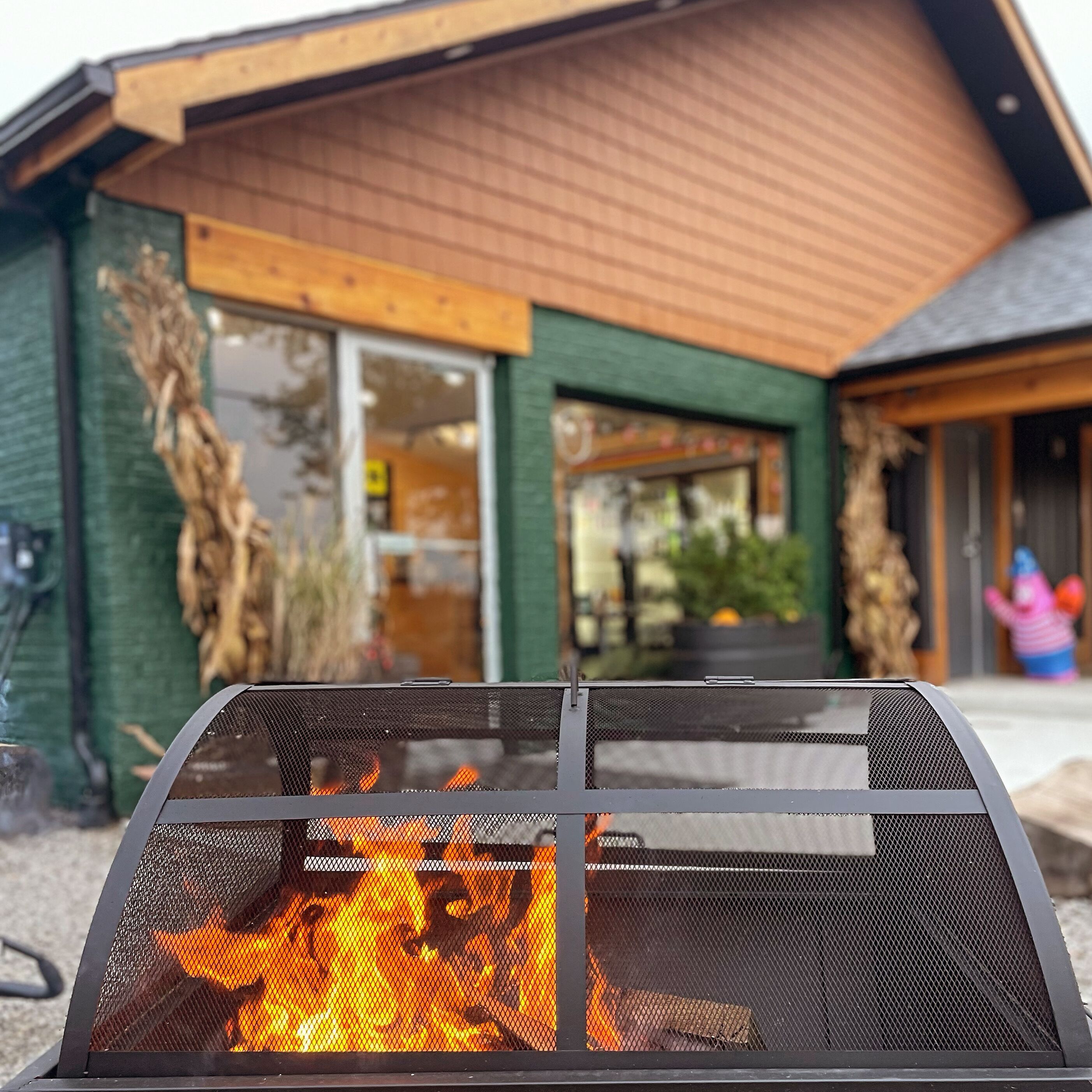 A fire pit in front of a building with a wooden exterior and large windows.
