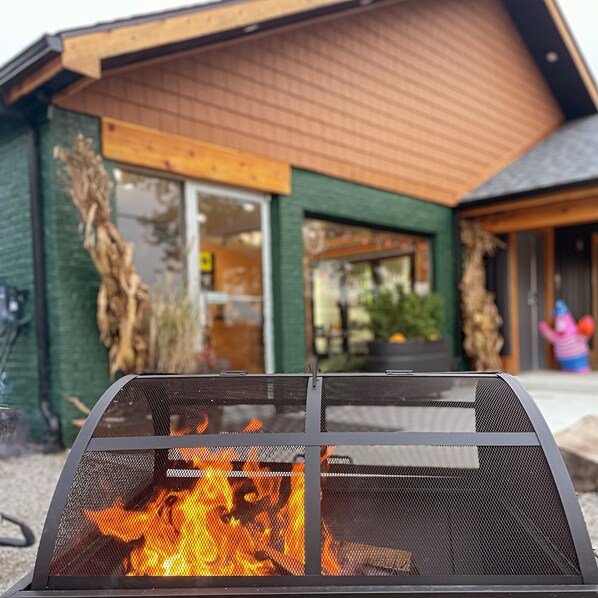 A fire pit in front of a building with a wooden exterior and large windows.