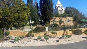 Ein Gebäude mit einer Stein-Fassade, einem markanten Turm und einem angelegten Garten mit verschiedenen Pflanzen.