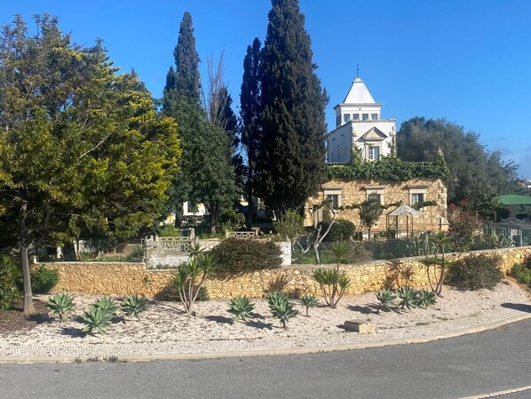 A building with a stone facade, a prominent tower, and a landscaped garden with various plants.