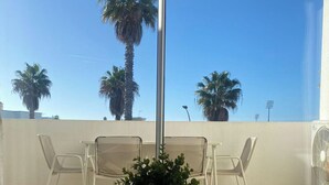Ein Balkon mit zwei weißen Korbstühlen, einem Tisch und einem Blumentopf.