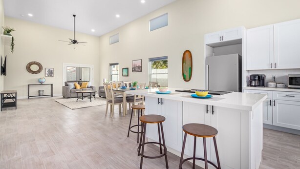 Una cocina moderna con armarios blancos, una isla grande con taburetes y una zona de comedor con sofá y sillas.