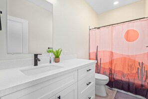A bathroom with a white vanity, a black faucet, a mirror, a white toilet, and a shower curtain with a desert landscape design. - 10 Min from Super Bowl, Shopping, NEW home, King Beds, Sleeps 10 (Peoria)