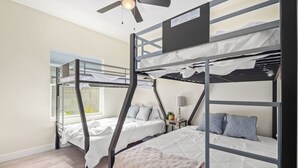 Habitación con literas, ventilador de techo, ventana con persianas y mesita de noche con lámpara.