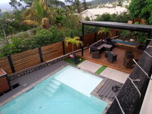 Un área de piscina en la azotea con terraza de madera, mobiliario exterior y vistas del paisaje circundante.