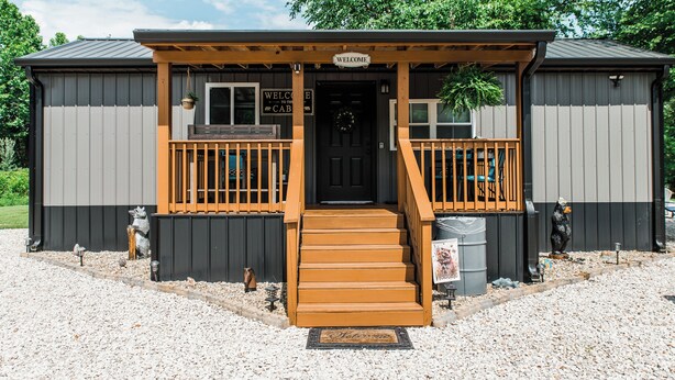 A cabin with a wooden porch, a welcome sign, and a black door. - New Tiny Lake Home (Salt Lick)