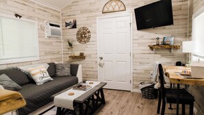 A cozy living room with a sofa, a coffee table, a TV, and a wooden floor. - New Tiny Lake Home (Salt Lick)