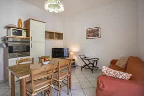 Un ambiente compatto con tavolo e sedie da pranzo, divano, televisione, forno a microonde e un piccolo mobiletto.