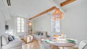 Un salon lumineux avec un canapé, une table à manger dressée pour deux personnes et un mur décoratif en pierre.