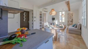 Une cuisine moderne avec un plan de travail gris, un coin repas avec une table et des chaises, et un salon avec un canapé et un mur d’accent en pierre.