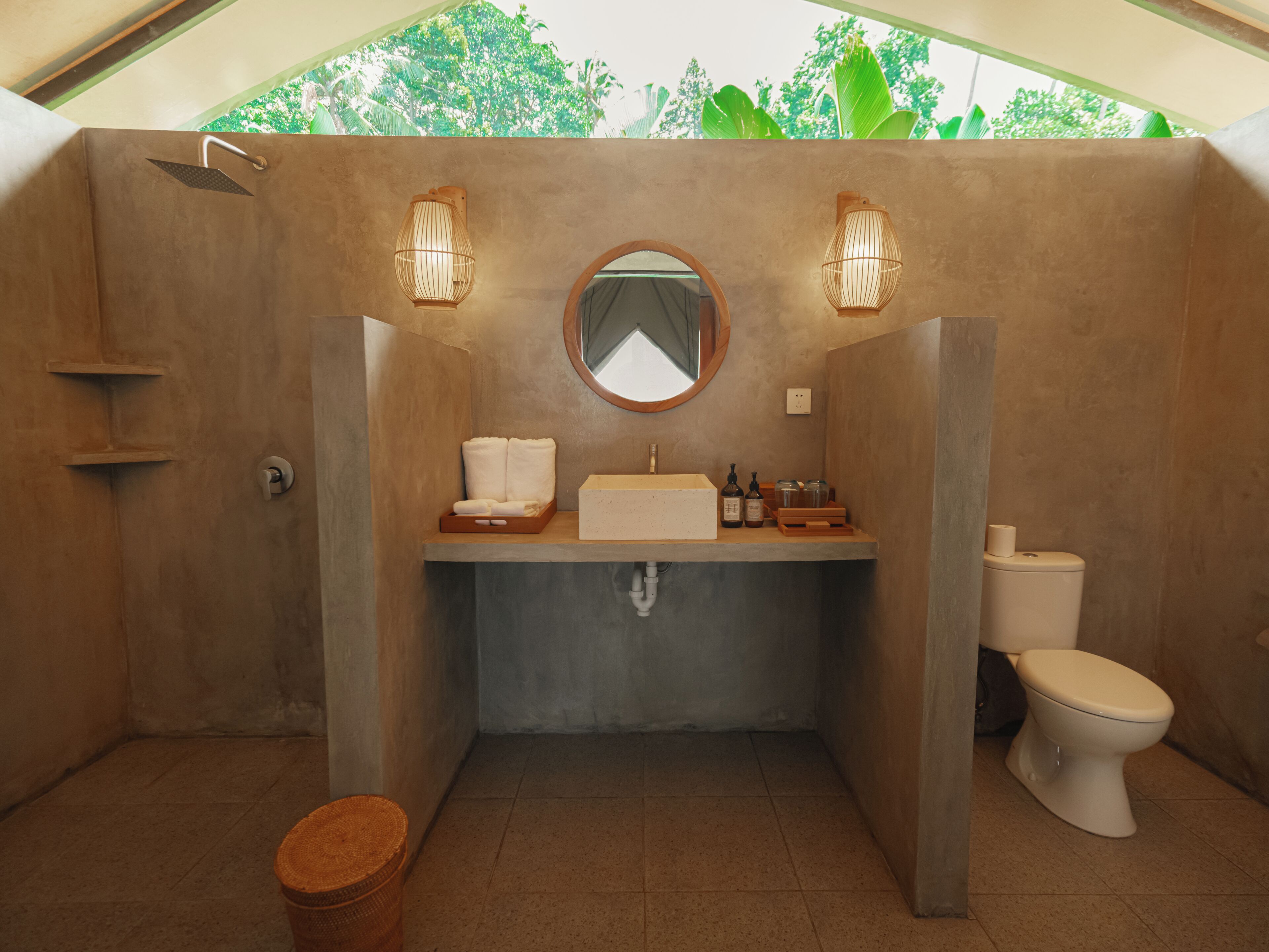 Une salle de bain comprenant un lavabo, un miroir, deux appliques murales, des toilettes et une petite poubelle.