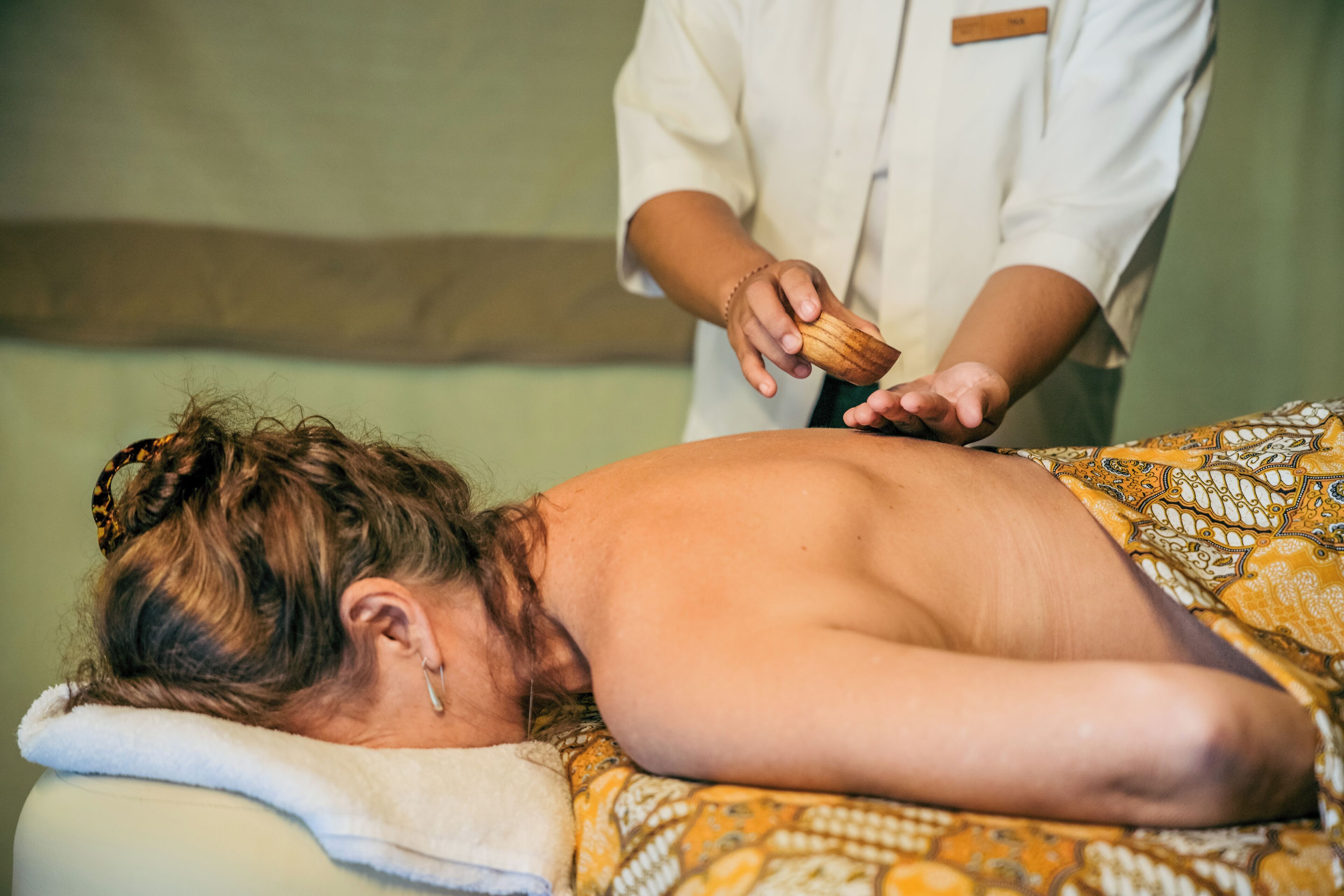A person receiving a massage in a room with a bed and a plain wall.