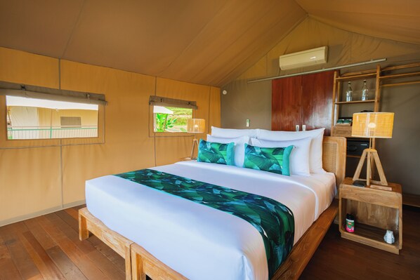A wooden-framed bed with a white and green bedspread, a bedside lamp, and a small wooden nightstand with a bottle. - Kaura Bali (Manggis)