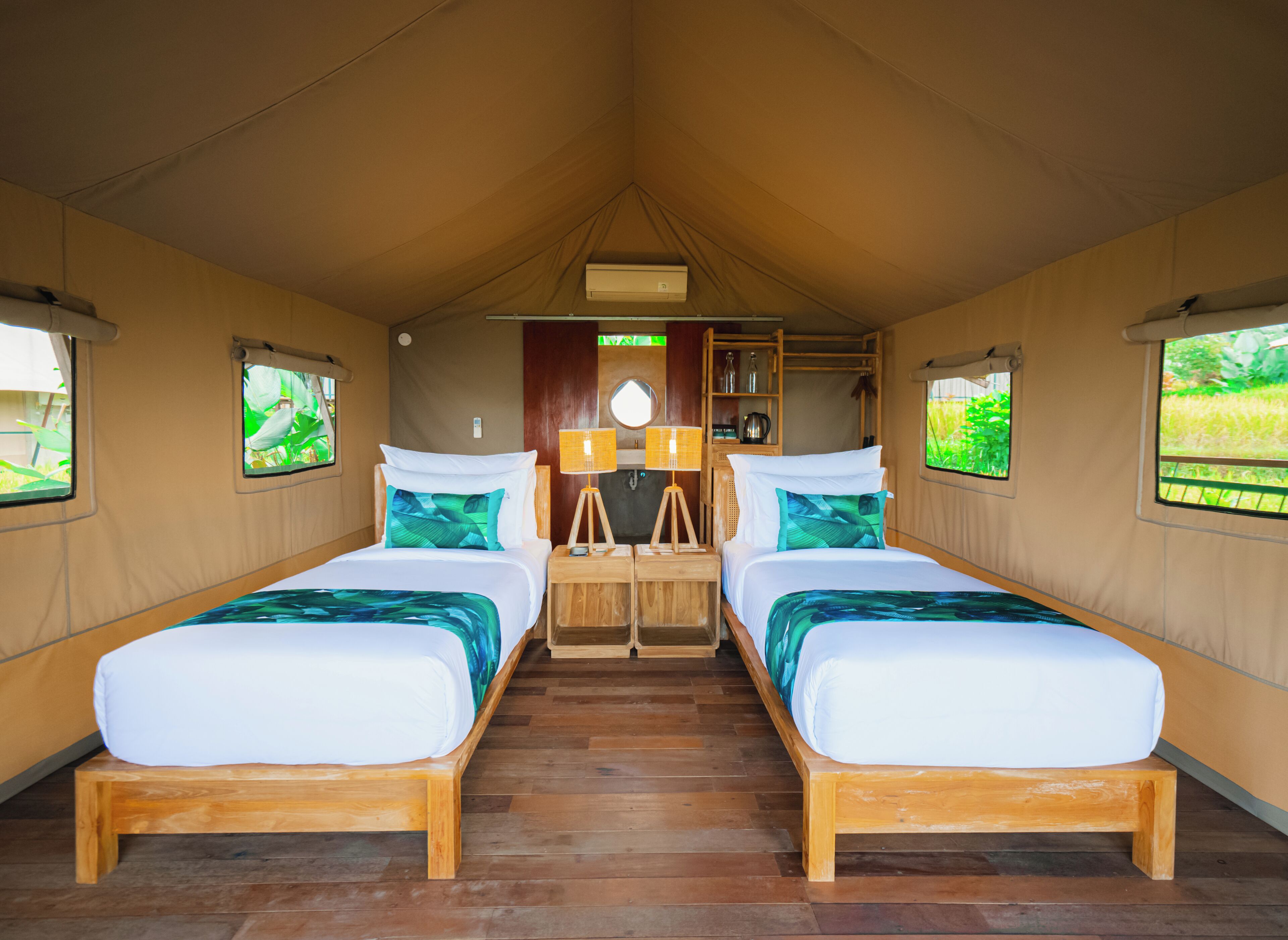 Acomodação em tenda com duas camas, uma mesa central e uma prateleira com objetos.