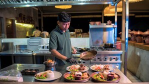 A chef preparing food in a commercial kitchen with stainless steel surfaces and various cooking equipment. - Kaura Bali (Manggis)