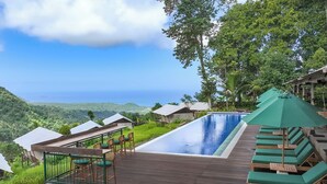 A poolside area with lounge chairs and a table, overlooking a mountainous landscape. - Kaura Bali (Manggis)