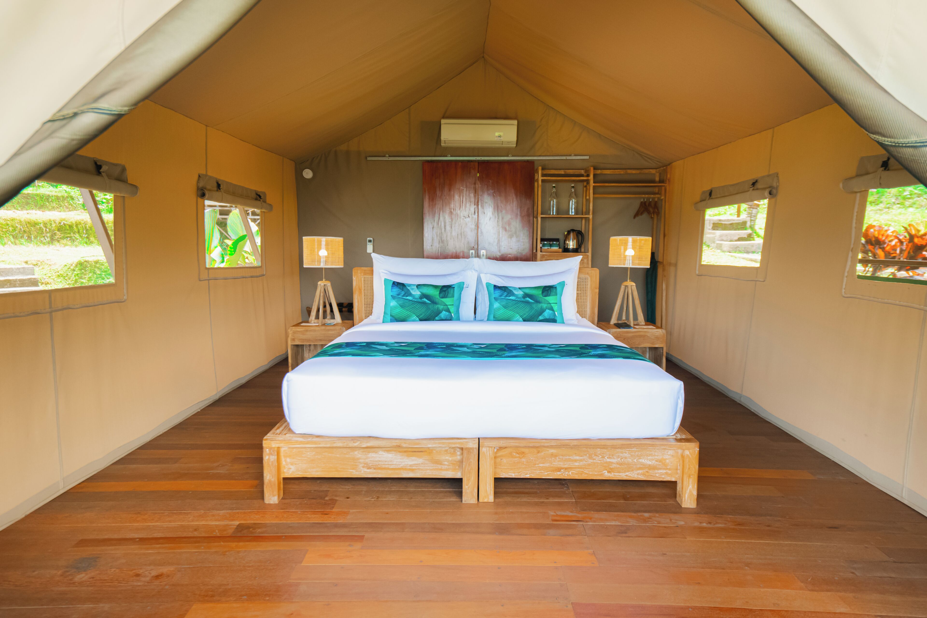 Quarto em acomodação tipo tenda, com cama, mesas de cabeceira, luminárias e uma estante com objetos.