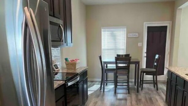 A modern kitchen with a stainless steel refrigerator, wooden flooring, and dark cabinetry. - Beautiful, Large 4 bedroom Home in Anna Tx (Anna)