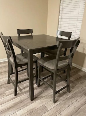 Une table à manger avec quatre chaises, un plancher de couleur claire et une fenêtre avec des stores.
