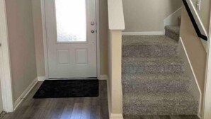 A hallway with a wooden floor, a white door, and a carpeted staircase. - Beautiful, Large 4 bedroom Home in Anna Tx (Anna)