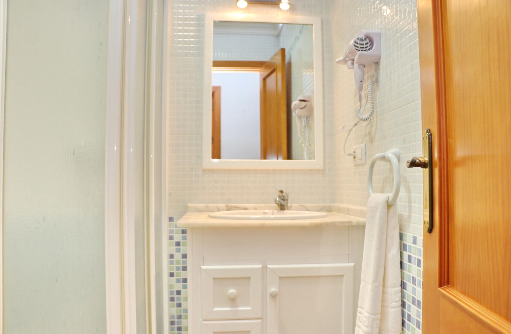 A bathroom with a white sink, a mirror above it, and a hairdryer mounted on the wall.