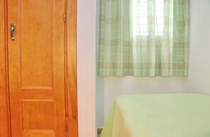 Um quarto com porta de madeira, uma cama com colcha verde e uma janela com cortinas verdes.