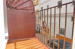 A balcony with a metal railing, a tiled floor, and a view of a building with windows and a car parked outside.