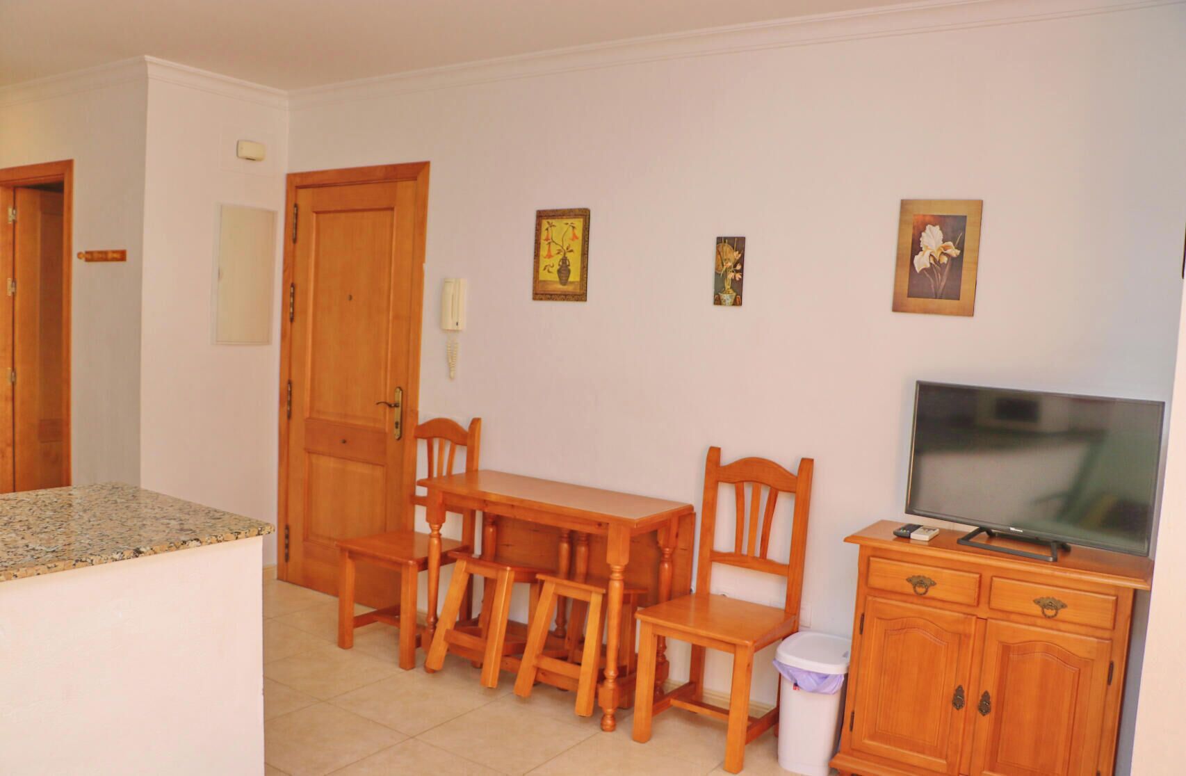 Un espacio habitable compacto con comedor, televisión y pequeña cocina.