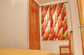 Un dormitorio con un armario de madera, una cama con colcha amarilla y una ventana con cortina a rayas.