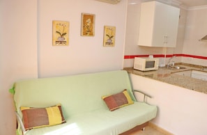 A room with a green sofa, a microwave, a sink, and three wall-mounted pictures of orchids.