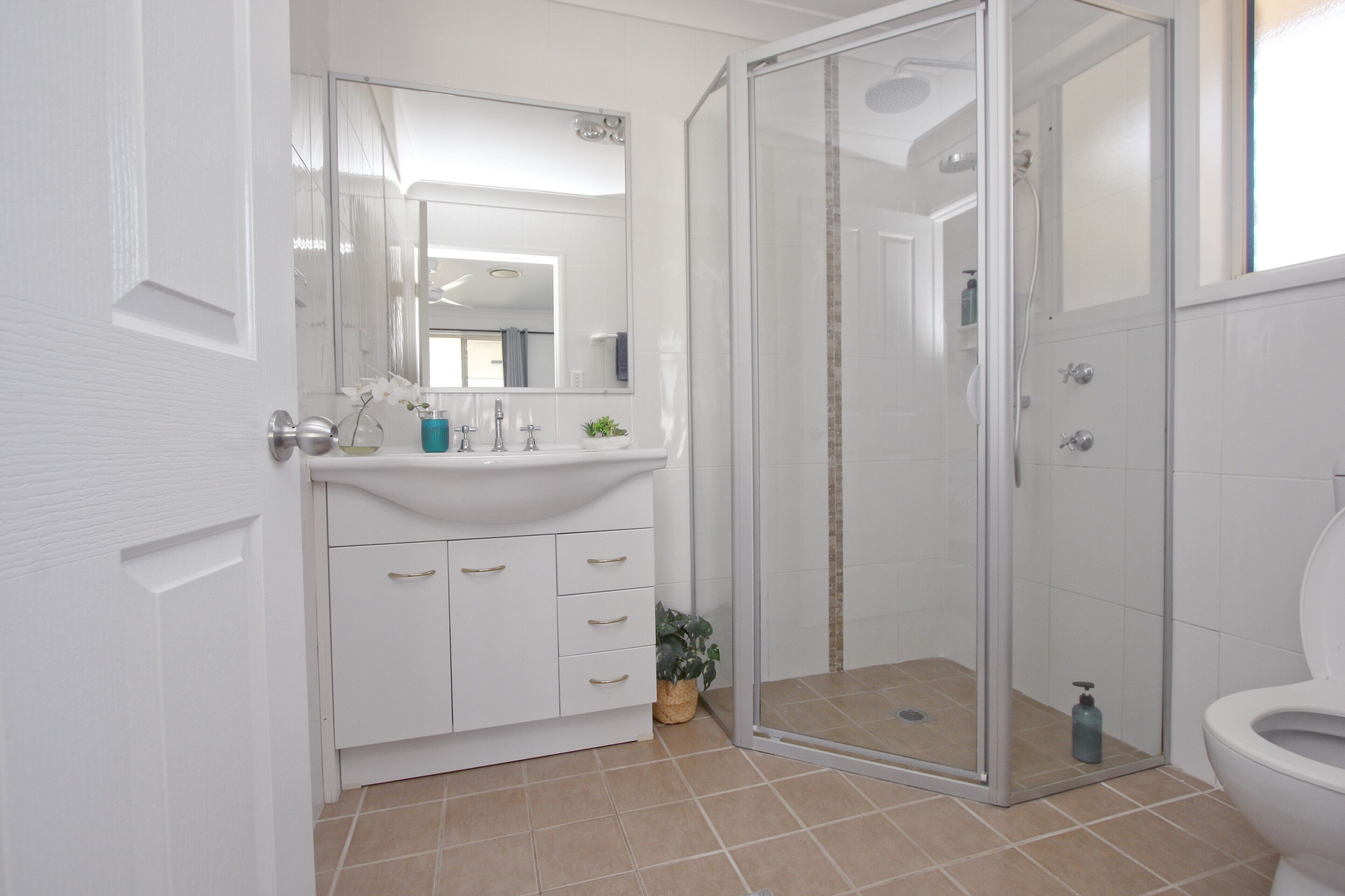A modern bathroom with a glass-enclosed shower, a white sink with a mirror above, and a toilet.