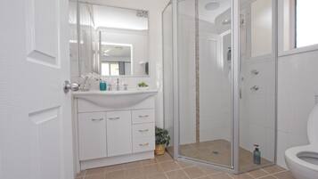A modern bathroom with a glass-enclosed shower, a white sink with a mirror above, and a toilet.