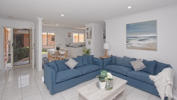Una sala de estar moderna con un sofá seccional azul, una mesa de centro con objetos decorativos y un cuadro del océano en la pared.