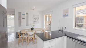 Una cocina moderna con armarios blancos, encimera negra y comedor con sillas y mesa de madera.