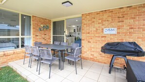 Un patio al aire libre con pared de ladrillo, una parrilla cubierta y una mesa de comedor con sillas.