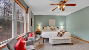 Une chambre à coucher avec un lit, deux tables de chevet, un ventilateur de plafond et une grande fenêtre.