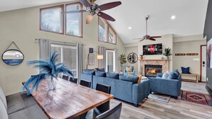 Un salon spacieux avec une cheminée, un coin repas avec une table en bois et un ventilateur de plafond.