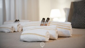 Una cama bien tendida con toallas blancas enrolladas y dos botellas de loción.