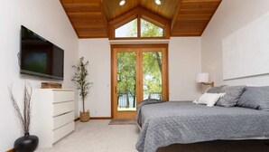 Une chambre à coucher avec un lit, une télévision, une commode, une plante et une grande fenêtre.