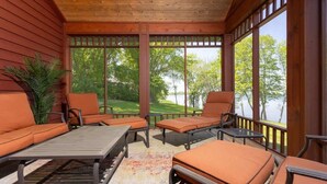 Un espace extérieur aménagé, abrité et doté de mobilier en bois, offrant une vue sur un lac.