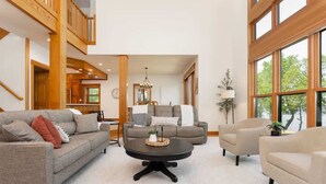 Un salon spacieux avec un plafond haut, une table basse centrale et une vue dégagée grâce à de grandes fenêtres.