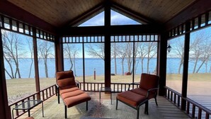 Un espace extérieur abrité, avec deux chaises et une table, donnant sur une étendue d’eau.