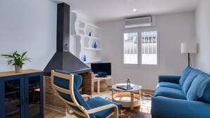 Ein modernes Wohnzimmer mit Kamin, einem blauen Sofa, einem Holzstuhl, einem Fernseher und einem Bücherregal.