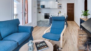 Ein modernes Wohnzimmer mit einem blauen Sofa, einem Essbereich mit Tisch für zwei Personen und einer Küche im Hintergrund.